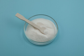 Glucono-delta-lactone, also known as gluconolactone. Pure GDL in Petri dish with ceramic spatula. Food additive E575. White powder, oxidized derivative of glucose. Acidity regulator, baking powder