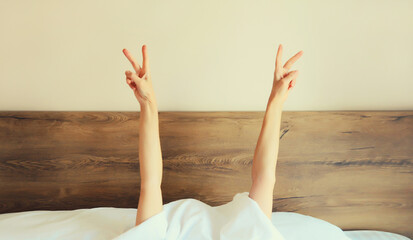 Cheerful lazy woman waking up after sleeping lying in bed stretching hands up in bedroom