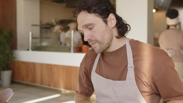 Small business owner in apron typing on laptop, reading receipts and taking notes on financial statement while calculating profit on bakery business