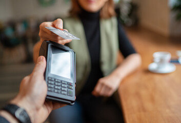 Young woman holding credit doing wireless bank payment with POS terminal process acquire at table in coffee shop cafe restaurant indoor. Focus on machine. Finance, restaurant industry, small business.