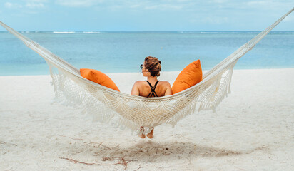 Young woman relaxing in wicker hammock on the sandy beach on Mauritius coast and enjoying wide...