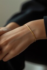 Thin gold bracelet on a woman's hand in a black jacket. Quiet luxury concept. 
