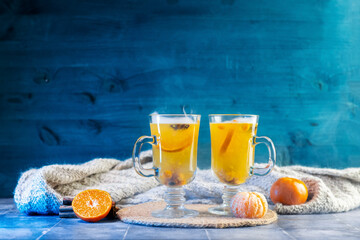 Two glass cups of warming fruit and berry tea with tangerine and sea buckthorn. Blue background.