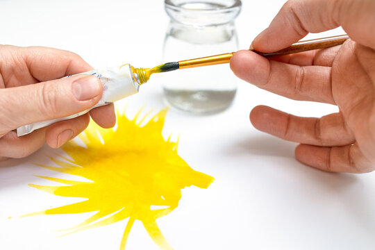Brush and yellow paints in the hands of the artist, a bright watercolor spot on the paper. With a brush he takes paint for painting on a white canvas, a glass transparent jar with water