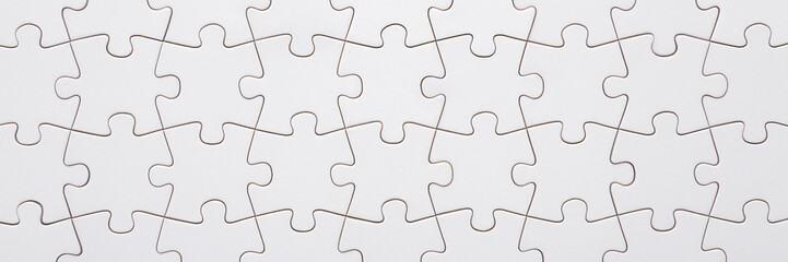Finished puzzle from different many white pieces. Jigsaw background. Closeup. Wide banner. Empty place for text. Top down view.