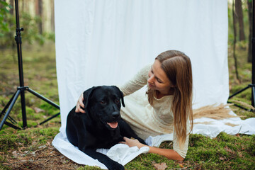 a woman in a white evening dress with sequins on a white background in the forest. dry yellow grass in the hands of a girl. eco photo shoot. a woman in a white dress with a black labrador dog 