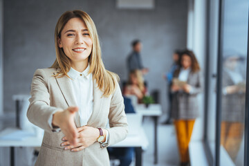 Head shot portrait smiling  businesswoman offering handshake, standing with extended hand in modern office, friendly hr manager or team leader greeting or welcoming new worker - obrazy, fototapety, plakaty
