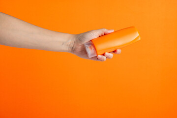 Shampoo bottle in hand isolated on orange background