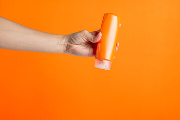 Shampoo bottle in hand isolated on orange background
