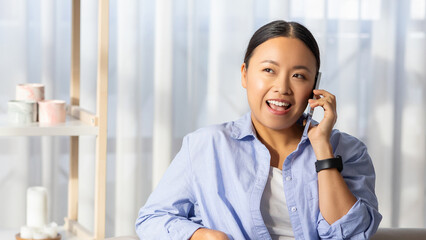 Positive young korean lady talking on phone, home interior