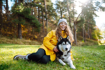 Beautiful young woman in a yellow coat walks in a park with her pet husky. A pet owner spends time with her dog. Concept of fun, entertainment.