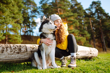 Beautiful young woman in a yellow coat walks in a park with her pet husky. A pet owner spends time...