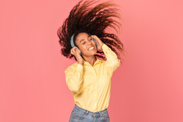 Happy woman dancing with headphones on pink background