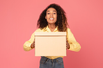 Young black woman smiles holding parcel on pink backdrop
