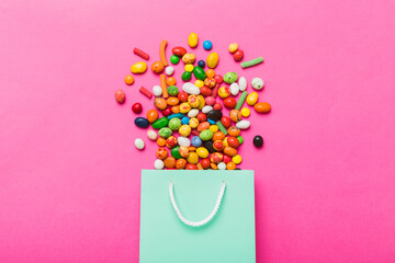 shopping paper gift bag in corner full of assorted traditional candies falling out on colored...