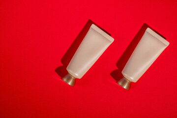 Plastic white tube for cream or lotion. Skin care or sunscreen cosmetic on red background.