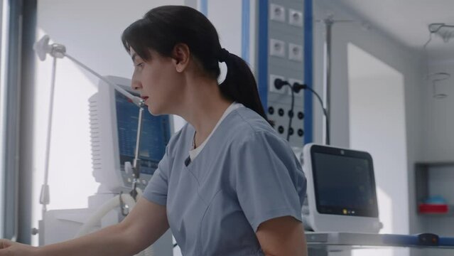 Emergency room with modern equipment in clinic. Elderly man in oxygen mask lies in bed after surgery. Nurse talks to old patient, uses hospital monitor. Intensive care department in medical facility.