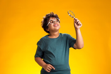 Child boy looking through magnifier over yellow background. Education and curiosity concept