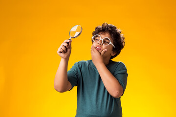 Child boy looking through magnifier over yellow background. Education and curiosity concept