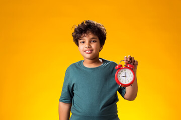 Child boy holding alarm clock over yellow background. Time management concept