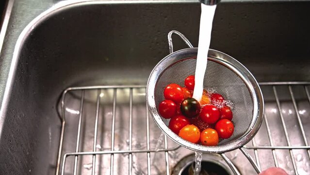 The video depicts the process of thoroughly rinsing vibrant cherry tomatoes in a metal strainer under running water.