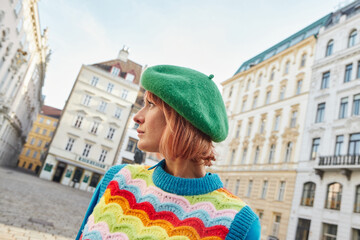 modern street fashion, stylish woman in beret and bright vest looking away on street in Vienna