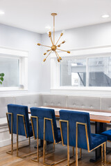 A modern, corner dining room detail with bench seating, a gold sputnik chandelier, blue chairs with gold legs surrounding a wooden table, and hardwood floors.