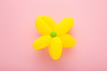 Beautiful flower head shape created from yellow balloon on light pink table background. Pastel color. Closeup. Top down view.