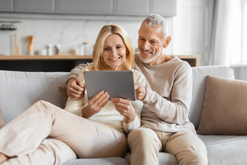 Excited smiling senior spouses using digital tablet computer at home