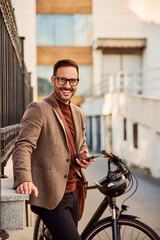 Portrait of a smiling businessman with a bicycle using a mobile phone.