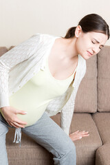 The expectant mother suffers from back pain and tries to sit on the sofa