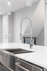 A kitchen faucet detail with a stainless steel apron sink, polished chrome faucet, and glass light...