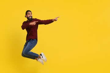 Fototapeta na wymiar Emotional excited millennial indian guy jumping, showing advertisement