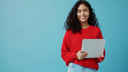 woman with curly hair is smiling and holding a laptop, wearing a red sweater, against a teal blue background