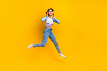 Fototapeta na wymiar Full length portrait of cheerful nice person jump hands touch headphones empty space isolated on yellow color background