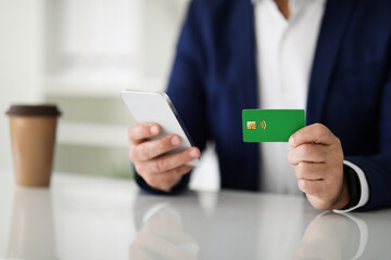 Close-up of a businessman's hands using a smartphone and holding a green credit card