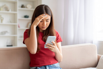 Concerned young asian woman touching forehead while reading message on mobile phone