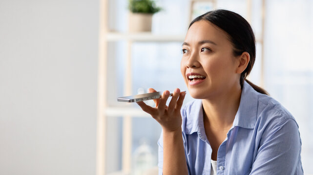 Asian woman recording voice message, using smartphone