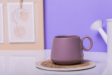 Obraz na płótnie Canvas A purple mug sits on a white table against a backdrop of a painting on a violet wall. Perfect for cozy café promotions or interior design inspiration.