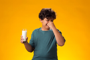 Dairy intolerant unhappy child boy holding glass of milk over yellow background. Lactose...