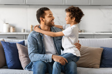 Affectionate African American father and preteen son embracing and smiling at home