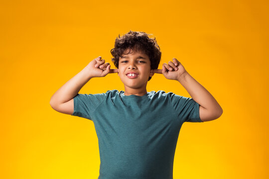 Kid boy covering ears over yellow background. Noise, stress and childhood concept