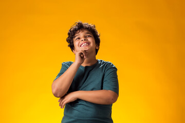 Thoughtful child boy holds chin on yellow background. Dreaming concept