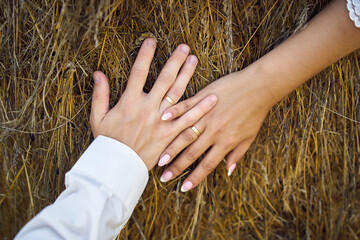 Close-up of hands of bride and groom with wedding rings holding each other and lying on hay bales