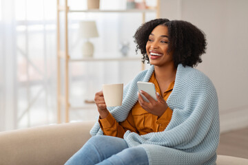 A joyful woman with natural curly hair, wrapped in a knitted blue blanket