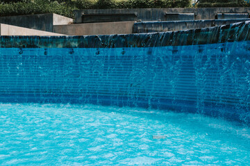 Fototapeta na wymiar The water flows along a large semi-circular pool. Stylish blue swimming pool in the park