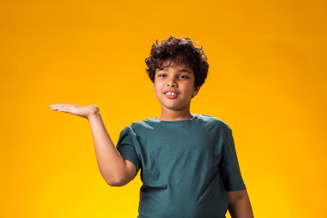 Smiling child boy pointing finger at something over yellow background. Positive emotions concept