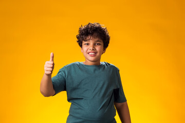 Smiling child boy showing thumbs up gesture over yellow background. Positive emotions concept