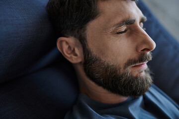 Fototapeta premium depressed anxious man with beard in casual attire lying on sofa during mental breakdown, awareness