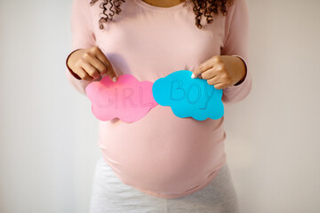 Pregnant woman holding pink and blue paper clouds with 'GIRL' and 'BOY'